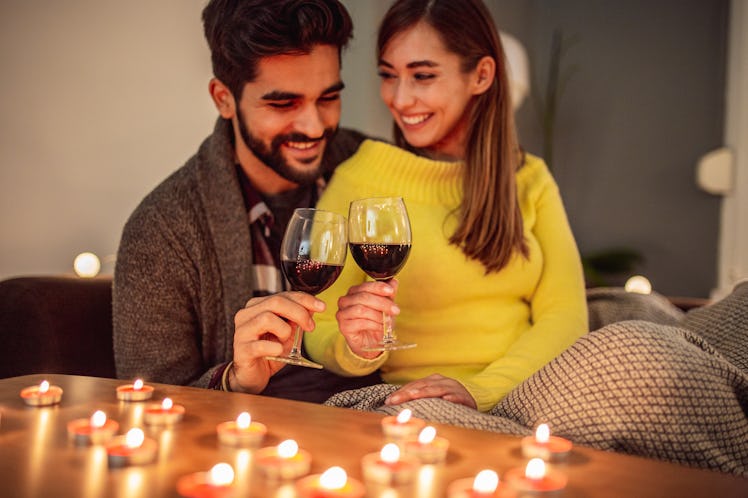 A happy couple snuggles on the couch and enjoys red wine during their at-home Valentine's Day date.