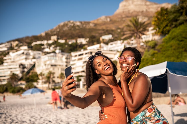 Two friends take a beach selfie under the sun.