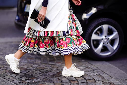 A woman walking and wearing a colorful dress and comfortable and chic sneakers