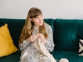 A woman crochets a blanket while sitting on her couch. 