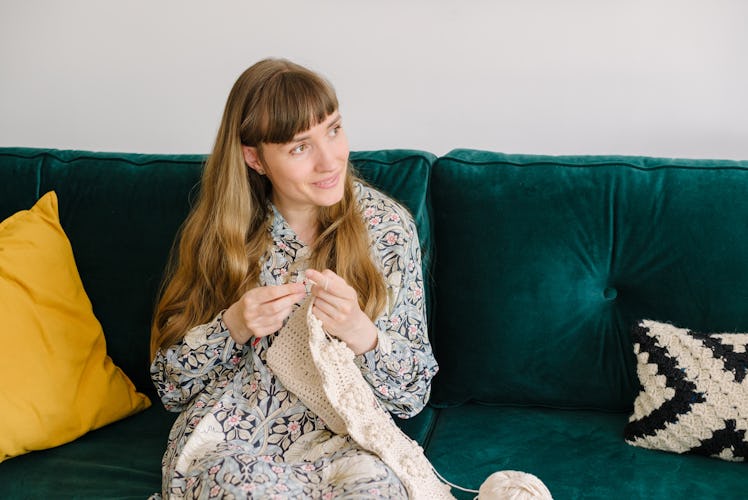 A woman crochets a blanket while sitting on her couch.