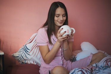 A happy woman in her striped pajamas looks into her coffee mug on her bed.