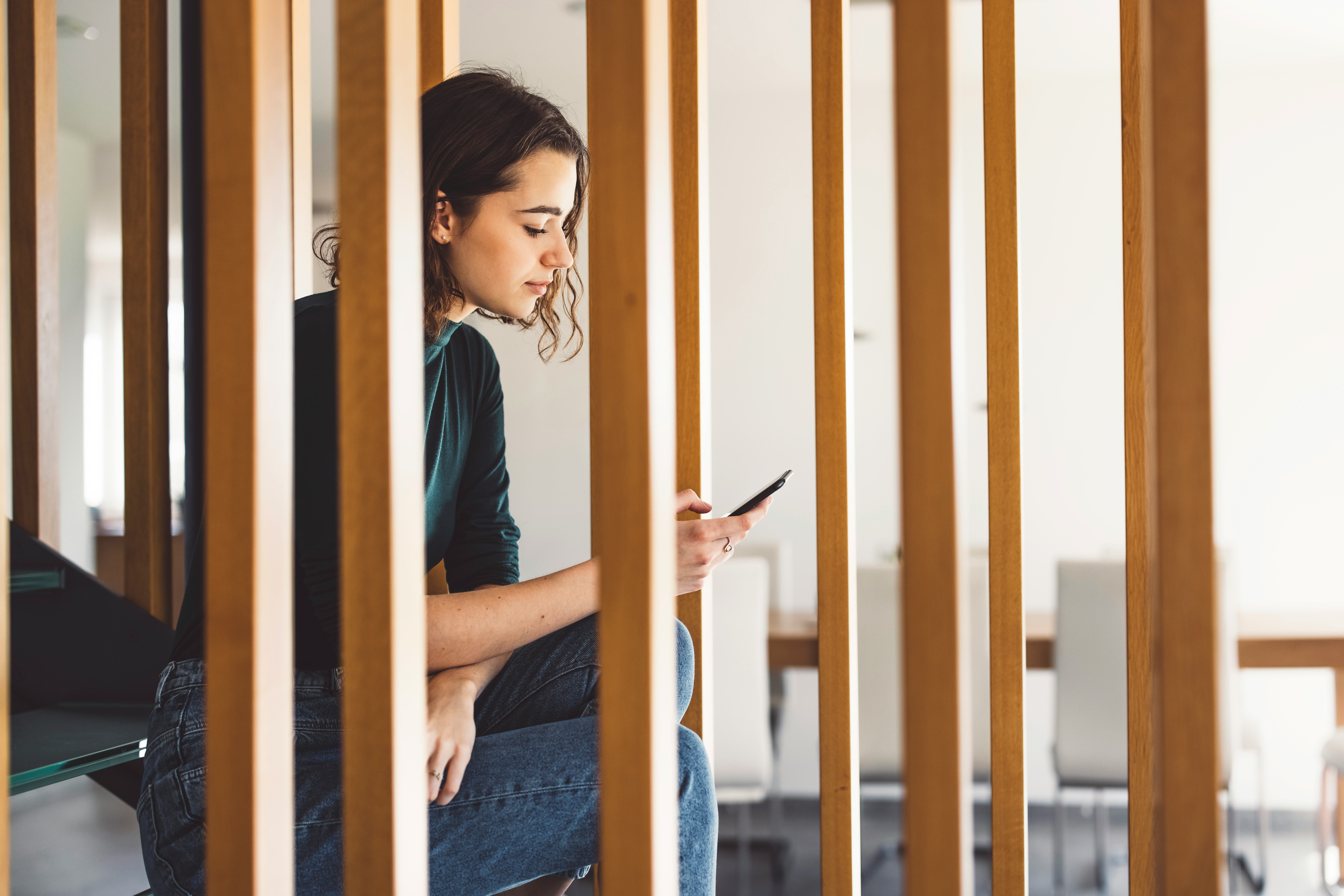 A woman sits on a staircase with her phone. Being constantly online creates a state of online vigila...