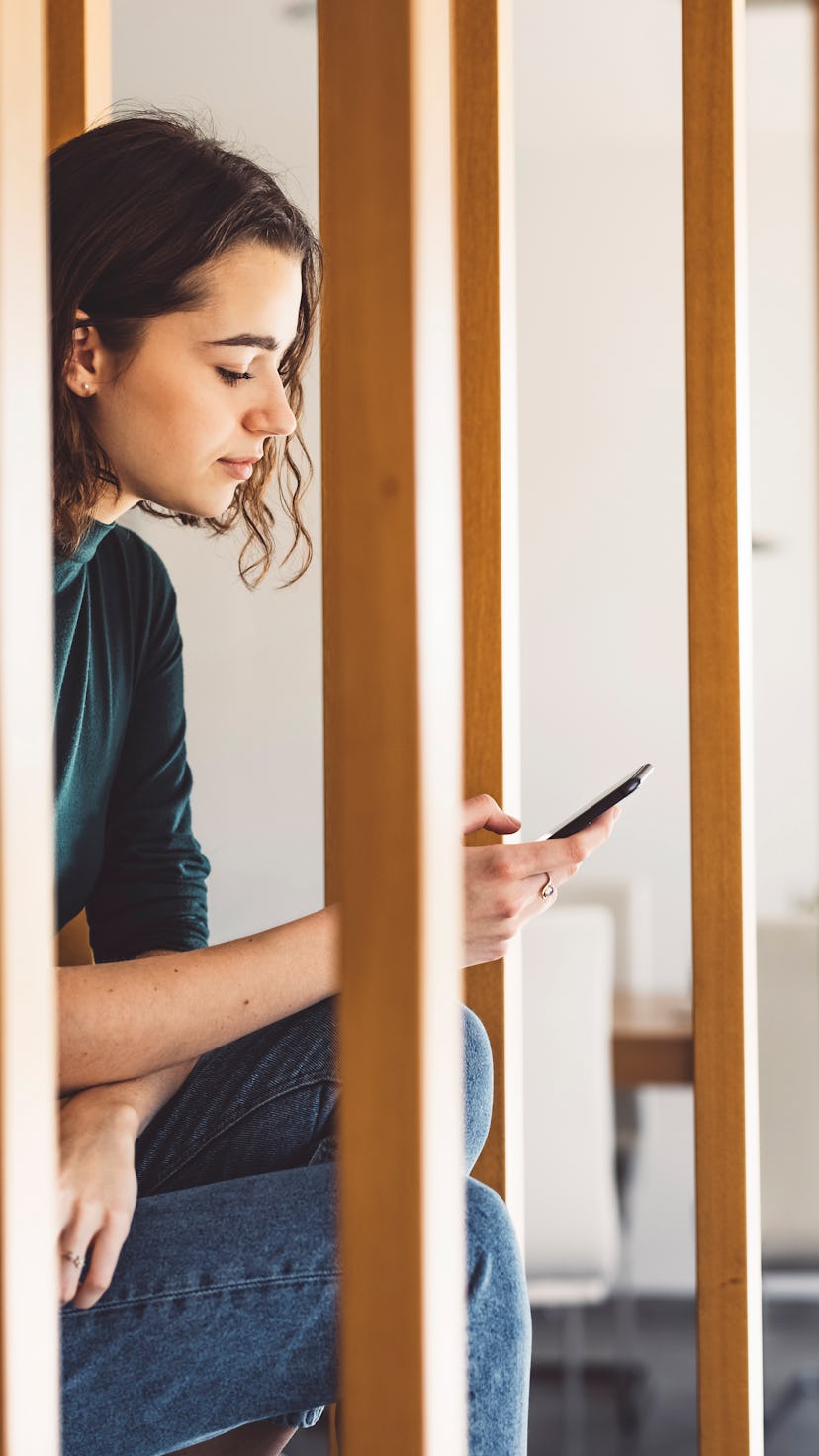 A woman sits on a staircase with her phone. Being constantly online creates a state of online vigila...