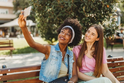 Two friends take a selfie on a bench in the summer.