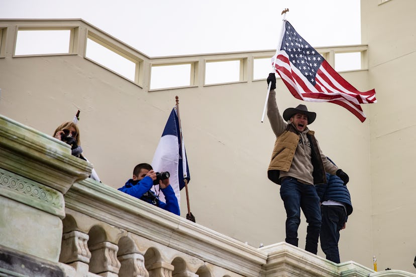 A man in a cowboy hat waves an american flag on the walls of the Capitol. Photos of Wednesday Jan 6 ...