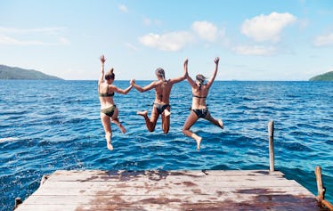 Three friends jump into a blue lake off a dock in the summer.