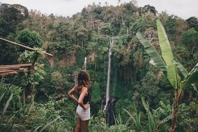 A young woman stands in front of a waterfall while on a jungle vacation before quarantine.
