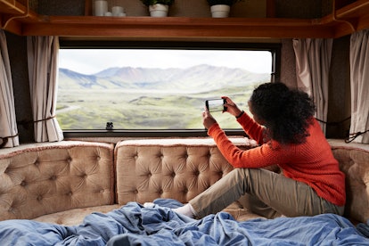 A woman takes a picture of the landscape while sitting in the back of a RV on vacation. 