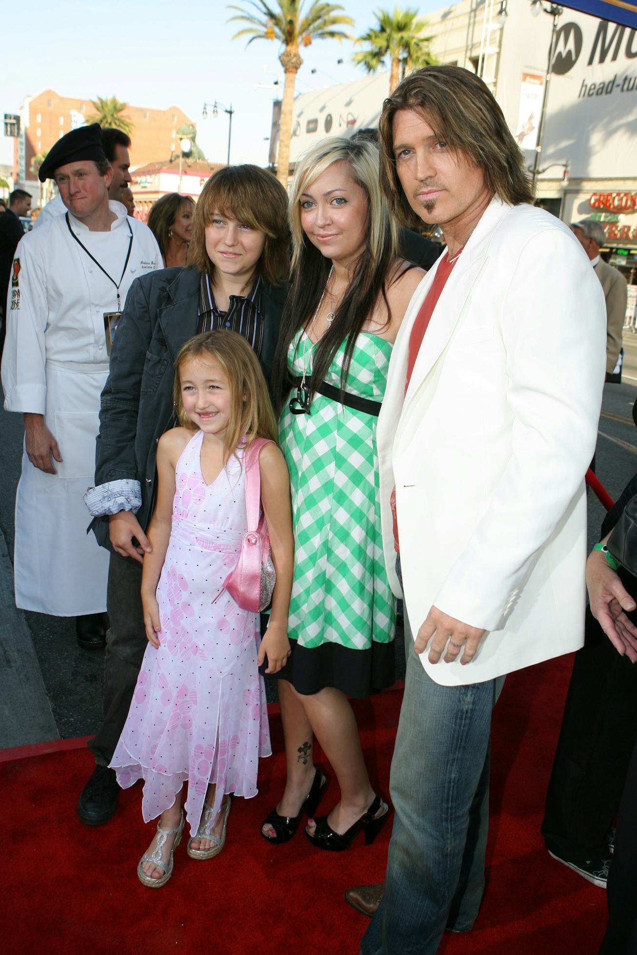 Noah Cyrus, in a long pastel pink dress next to Billie-Ray Cyrus, Brandi Cyrus, and Braison Cyrus on...