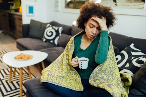 A woman in a blanket holds her head after doing dry january and getting a headache.