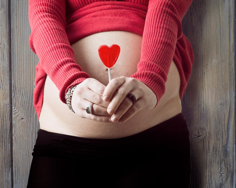 woman holding heart in front of belly for valentine's day pregnancy announcement ideas