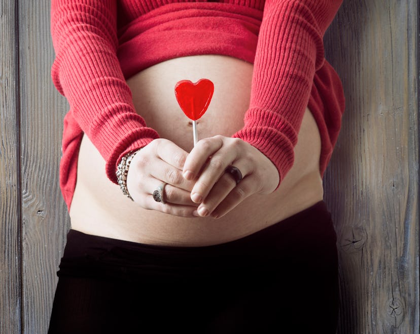 woman holding heart in front of belly for valentine's day pregnancy announcement ideas 