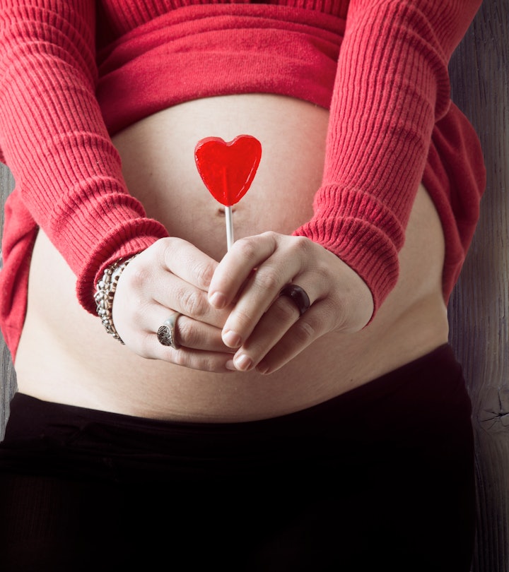 woman holding heart in front of belly for valentine's day pregnancy announcement ideas 