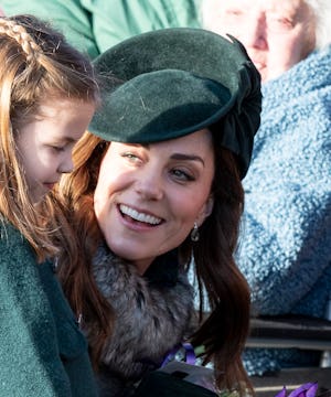 Kate Middleton wears a forest green hat and coat as she crouches down to speak with Princess Charlot...