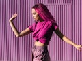A woman with pink hair wearing a pink cropped t-shirt and pink sweatpants dances in front of a pink ...