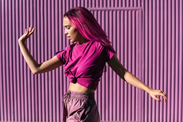 A woman with pink hair wearing a pink cropped t-shirt and pink sweatpants dances in front of a pink ...