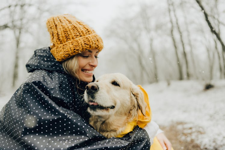 A young woman snuggles with her dog while playing in the snow.
