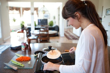 A happy woman flips a tortilla in a pan in her bright kitchen before filling it with veggies.