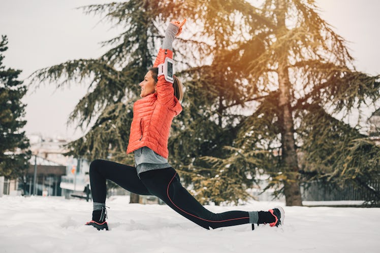 A young woman does winter-themed yoga in her backyard while wearing activewear.