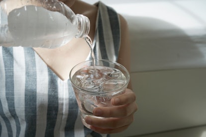 A woman in a striped jumpsuit pours water into a glass. Here's how dry january can cause headaches.
