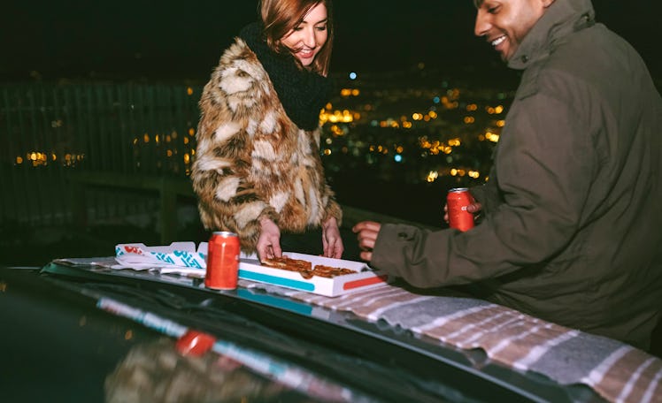 A happy couple enjoys a pizza on top of a car.