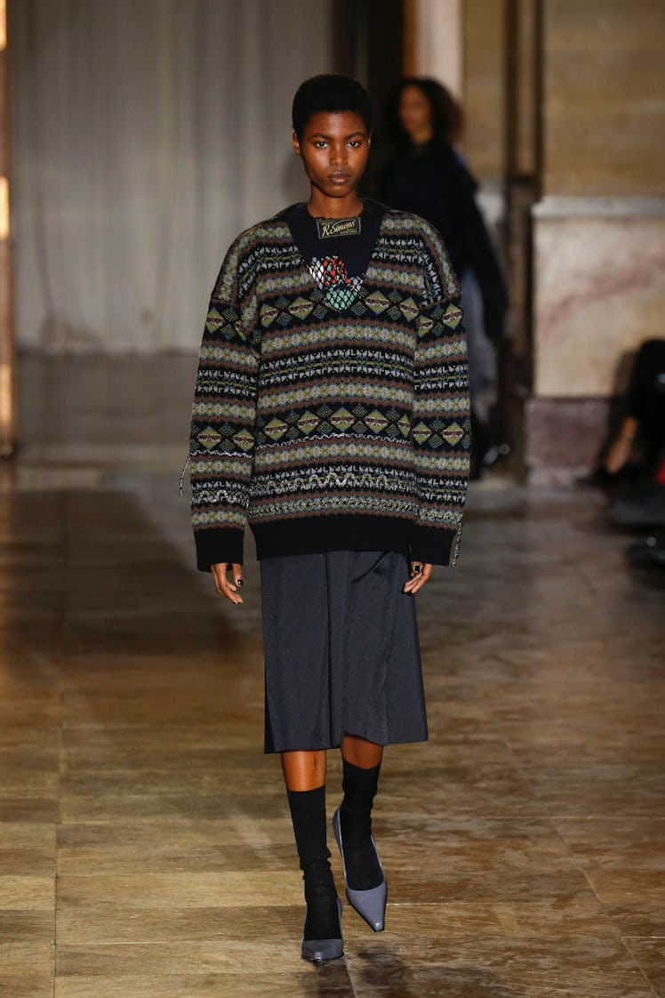A model walking in a black sweater and black skirt at the Raf Simons Ready to Wear Spring/Summer 202...