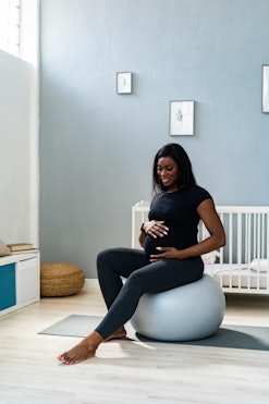 Image of a pregnant person, sitting in a nursery atop an exercise ball.
