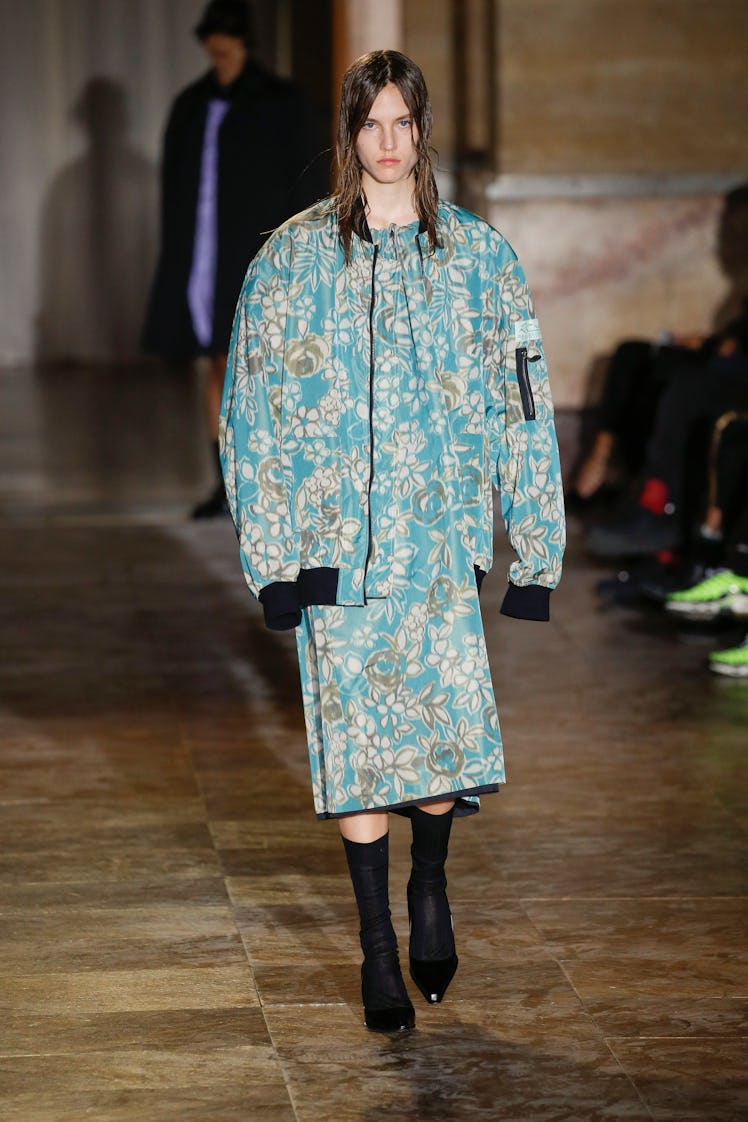 A model walking in a green floral jacket and dress at the Raf Simons Ready to Wear Spring/Summer 202...