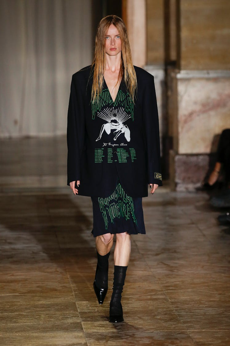 A model walking in a black-green blazer and skirt at the Raf Simons Ready to wear Spring/Summer 2022...