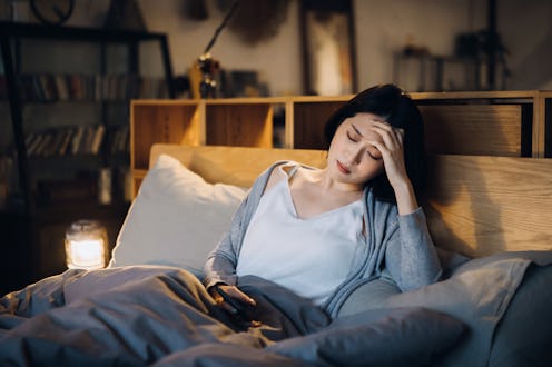 Young Asian woman feeling sick and suffering from a headache, lying on the bed and taking a rest at ...