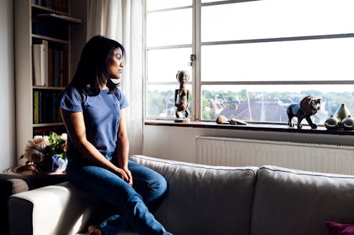 A woman sitting in her living room and looking through a window whose loneliness is affecting her me...