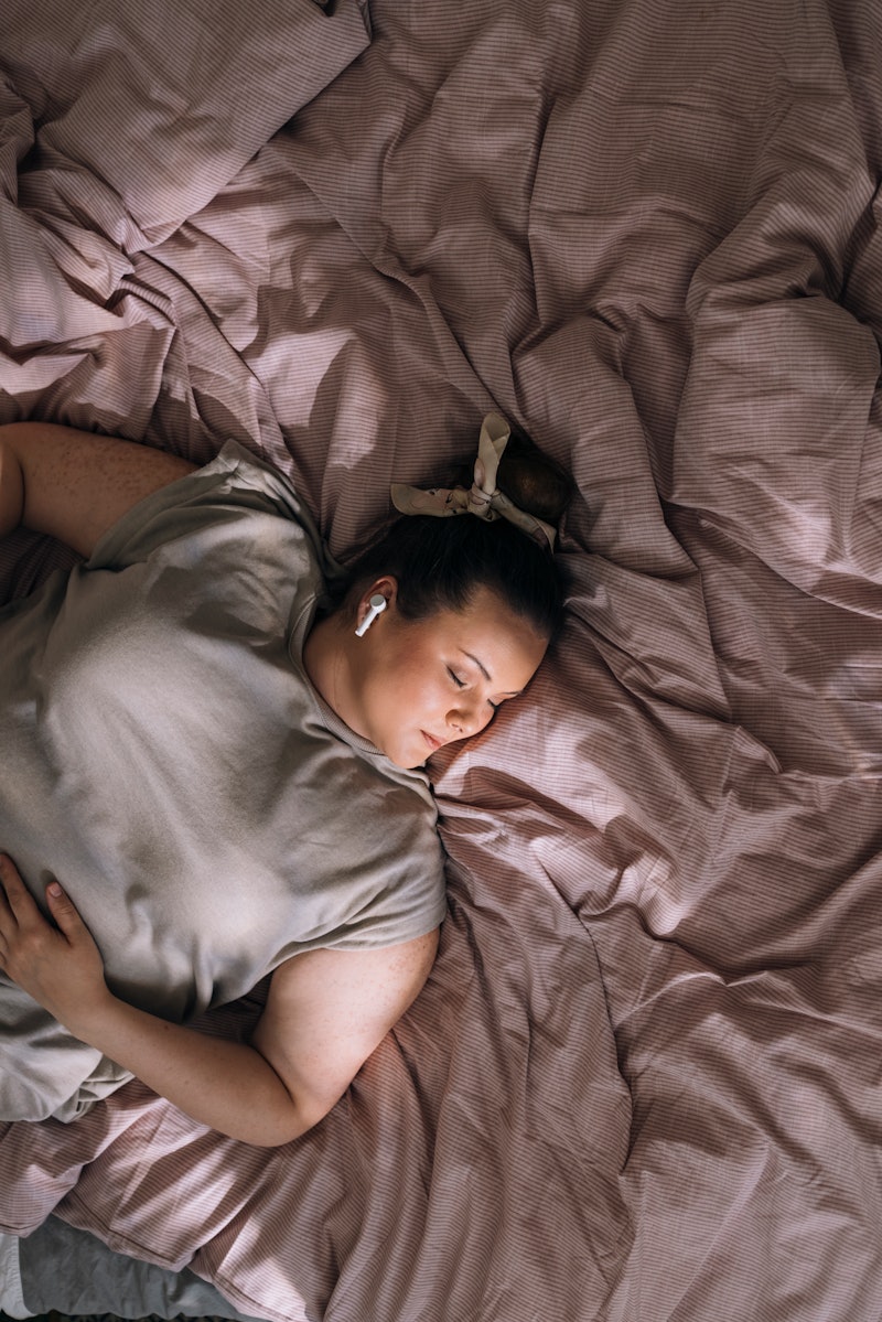 A young overweight Caucasian woman with earphones listening to music while sleeping