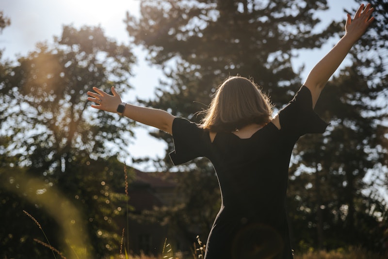 Back view of young woman with arms outstretched feeling free in nature