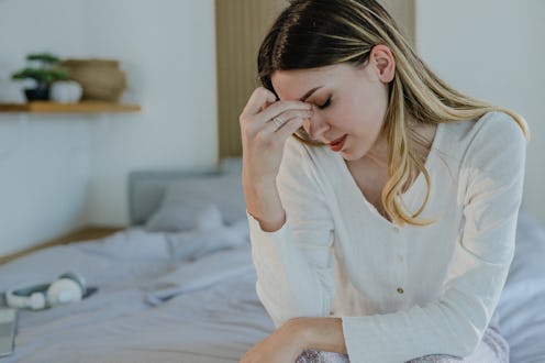 A sad young woman in bed suffers from depression and she is having a headache