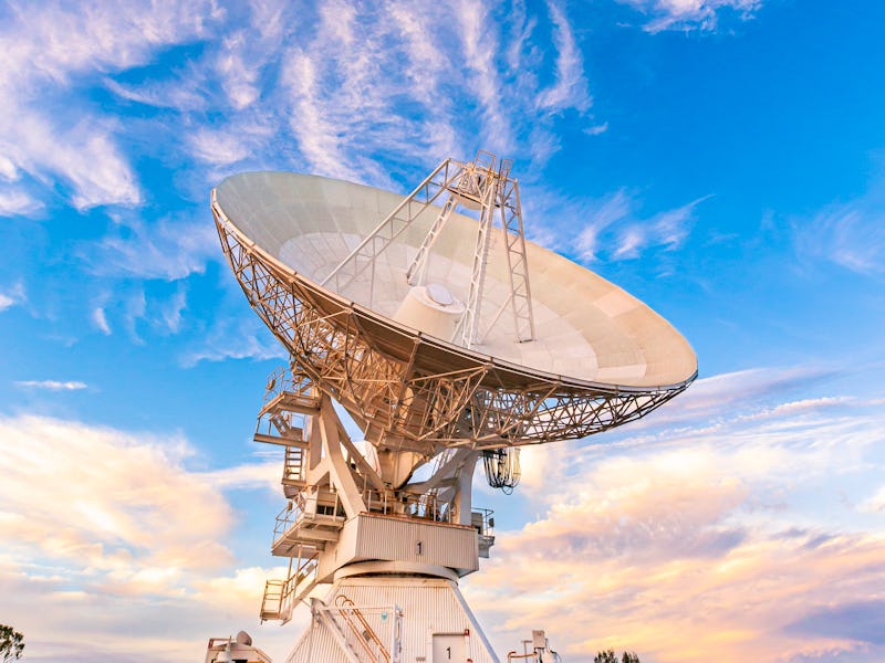 Portrait view of a Narrabri Radio Telescope at dusk, with moody blue sky and cloud background.