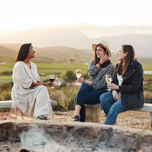 Shot of three women drinking wine while sitting by a fire pit