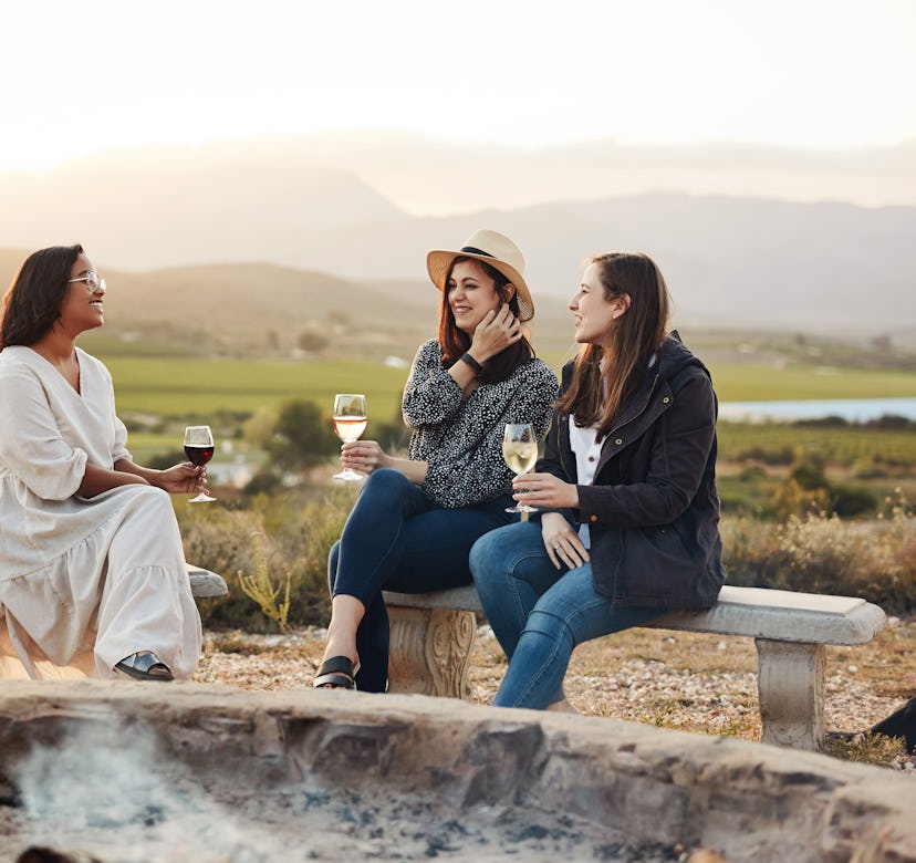 Shot of three women drinking wine while sitting by a fire pit