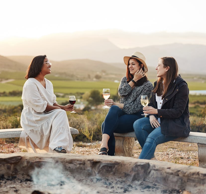 Shot of three women drinking wine while sitting by a fire pit