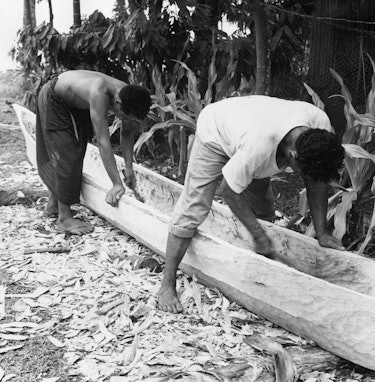 circa 1955:  Two men carving out a dugout canoe from a solid log in Western Samoa.  (Photo by John T...