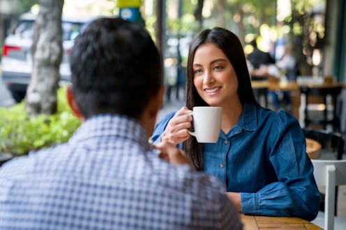 Beautiful Latin American woman on a date at a cafe smiling while drinking a cup of coffee