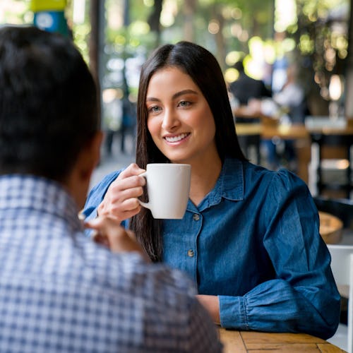 Beautiful Latin American woman on a date at a cafe smiling while drinking a cup of coffee