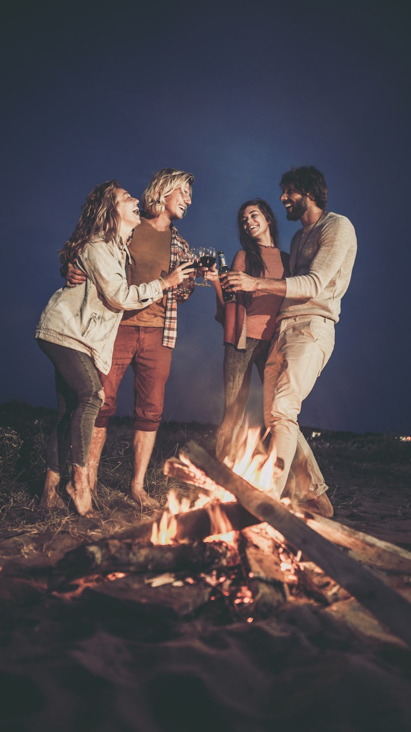 Friends having fun while toasting by the bonfire on the beach at night.