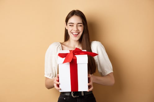 Happy smiling woman laughing, holding gift box from lover, enjoying romantic date on Valentines day,...
