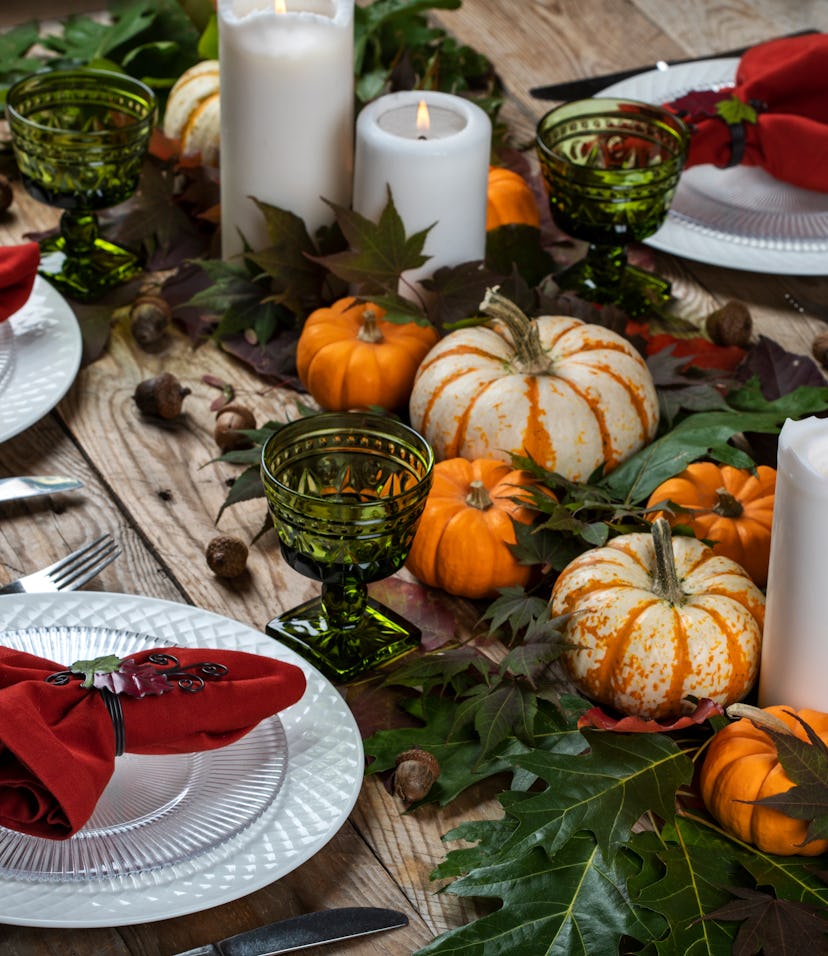 Autumn dinner. Autumn decor, white candles, autumnal leaves, white porcelain on a wooden table.