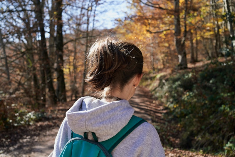 Rear view of a girl who uses an aquamarine color backpack and walk into a beech. A girls uses an aqu...