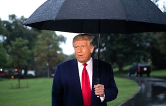 US President Donald Trump holds an umbrella as he speaks to the media under the rain prior to depart...