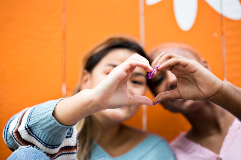 Young women bond together while peeking through a heart they made with their hands (focus on hands)