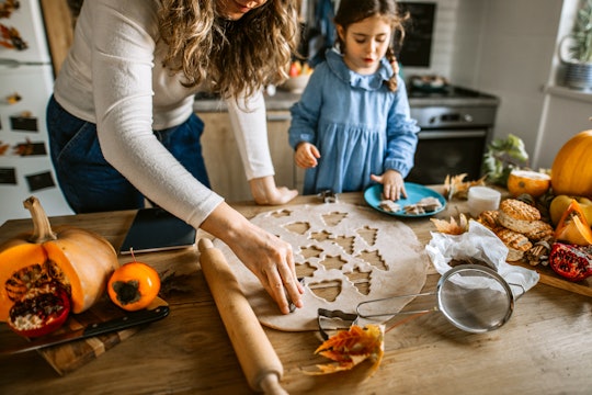 Young woman and her little cute daughter are making thanksgiving cookies in kitchen