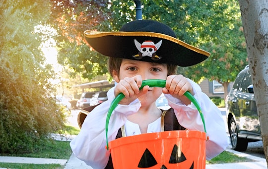 Pensive smiling little boy wearing a halloween pirate costume looking at the camera holding a Jack o...